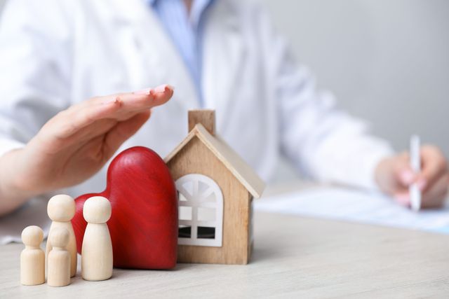 Figurines représentant une famille, une maison en bois et un cœur rouge protégés par une main