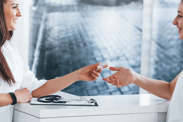 Une professionnelle de santé remet un médicament à une patiente au comptoir d'un cabinet